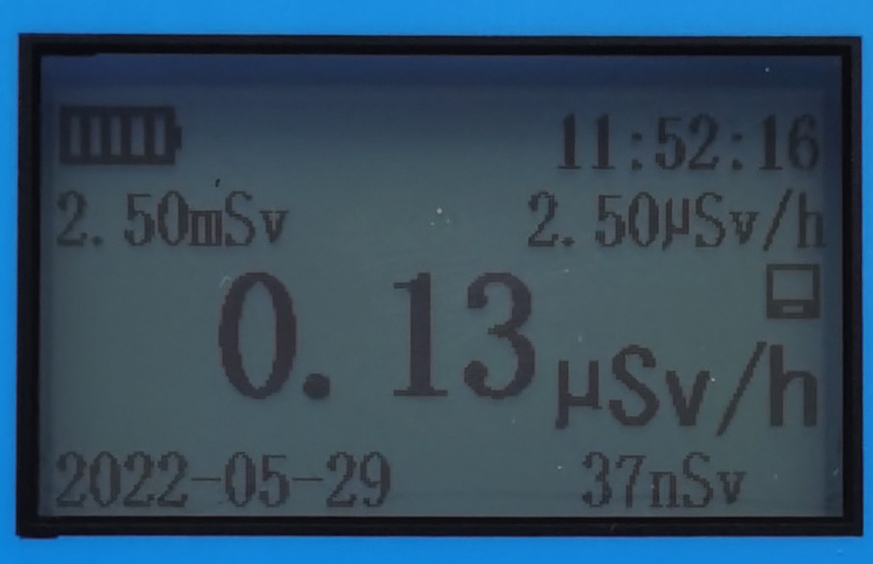 Close-up of a handheld radiation meter screen: 0.13 μSv/h in large digits, 37 nSv lower right, 2.50 mSv upper left, 2.50 μSv/h upper right